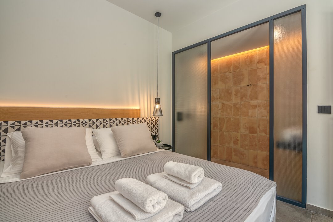 Intimate guest bedroom with queen bed, warm ambient lighting, and minimalist Mediterranean design at Nusa Gramvousa, Crete