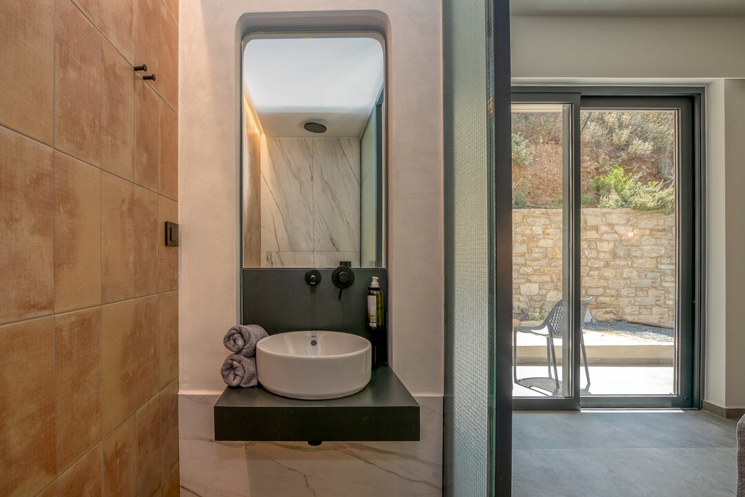Modern bedroom with direct bathroom access, frosted glass partition, and natural wood closet at Nusa Gramvousa villa, Crete