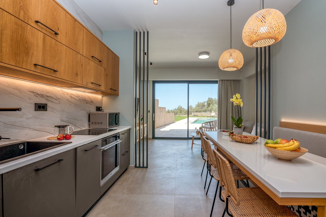 Modern fully-equipped kitchen with stainless steel appliances, marble backsplash, and oak cabinets at Nusa Gramvousa villa, Crete